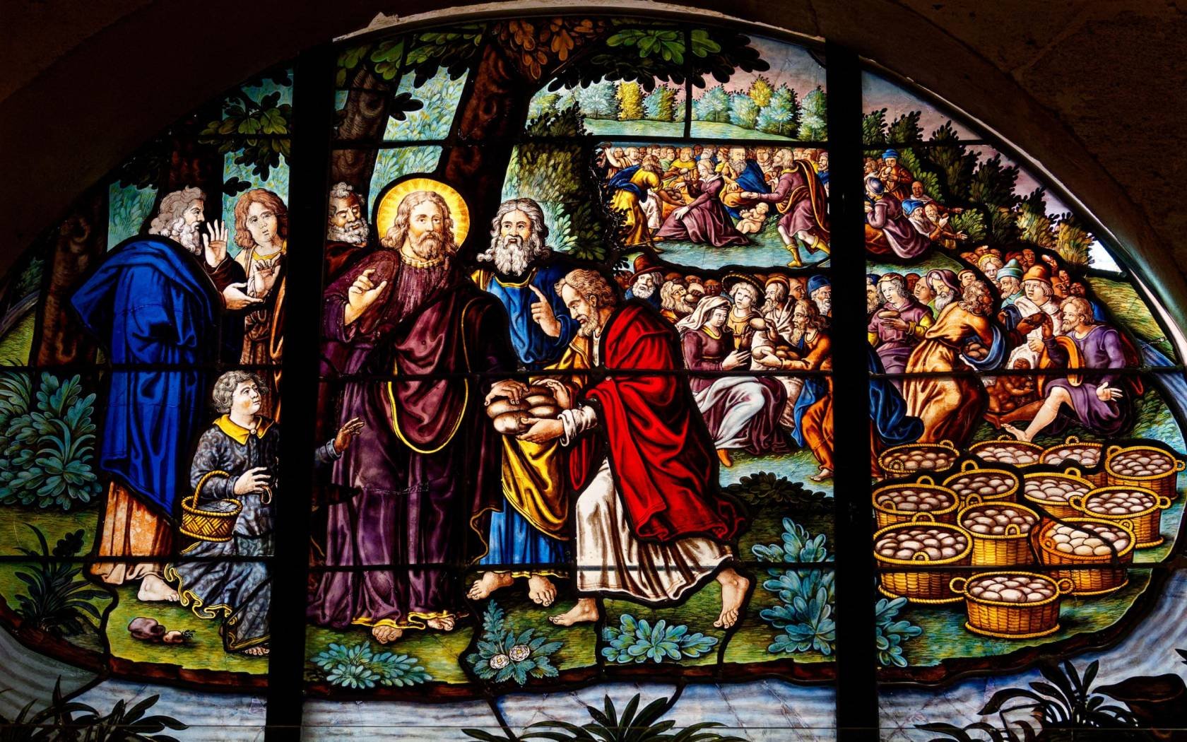 A stained glass of Jesus multiplying loaves and fish.