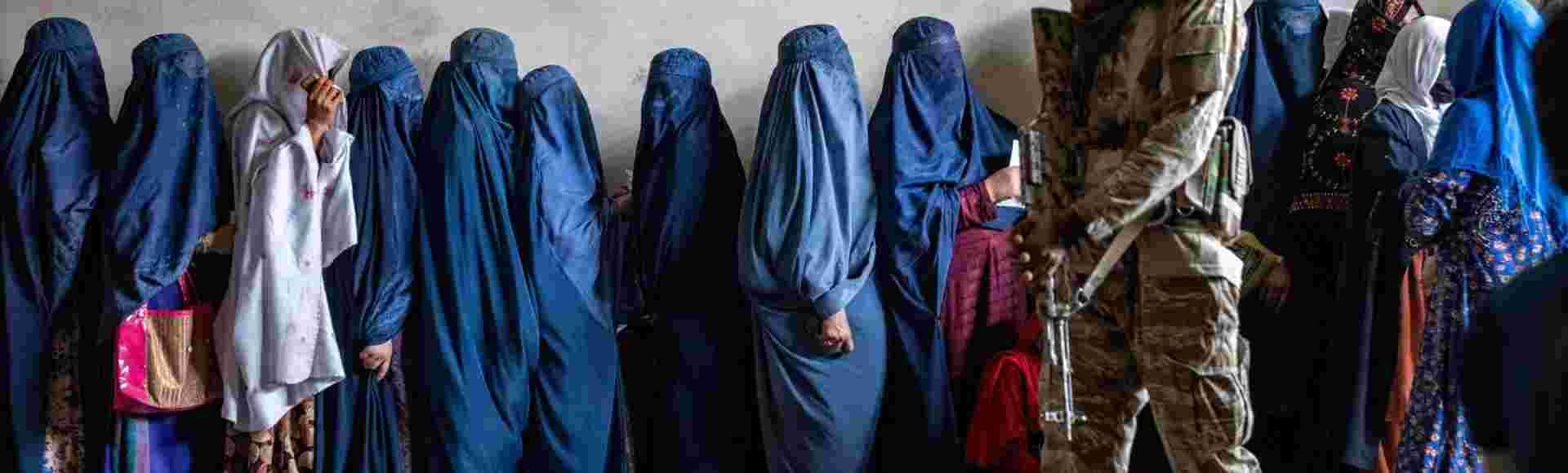 A Taliban fighter stands guard as women wait to receive food rations distributed by a humanitarian aid group in Kabul, Afghanistan, May, 2023.