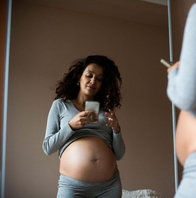 Reflection of pregnant woman taking selfie on smart phone at home