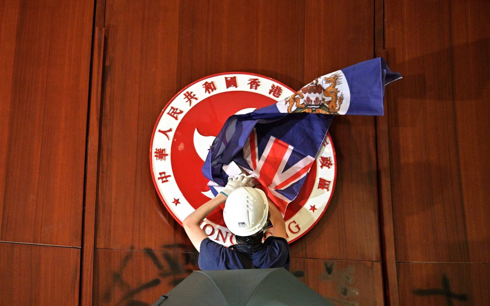 A protester attempts to cover the Hong Kong emblem with a British colonial flag after they broke into the government headquarters in Hong Kong in June 2019, the 22nd anniversary of the city's handover from Britain to China.