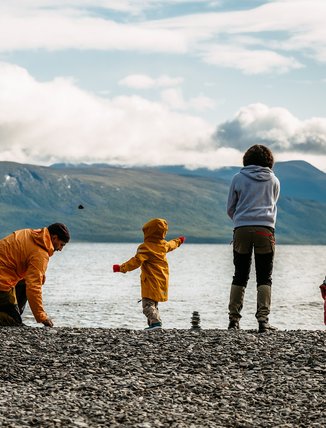 A family with children is throwing sandwiches on the rocky beach at Torneträsk and Silverfallet