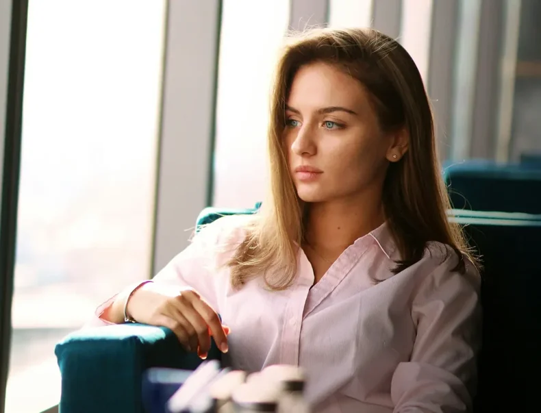 En kvinna i skjorta sitter och tittar ut genom fönstret på ett kontor.