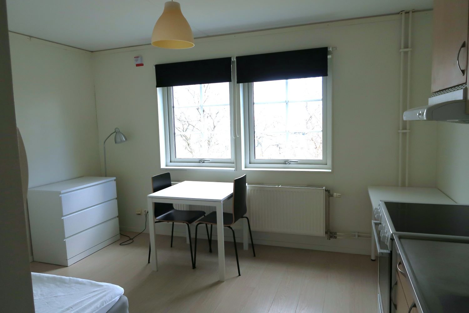 Studentroom with chest of drawers, table, chairs, kitchen area with stove top.