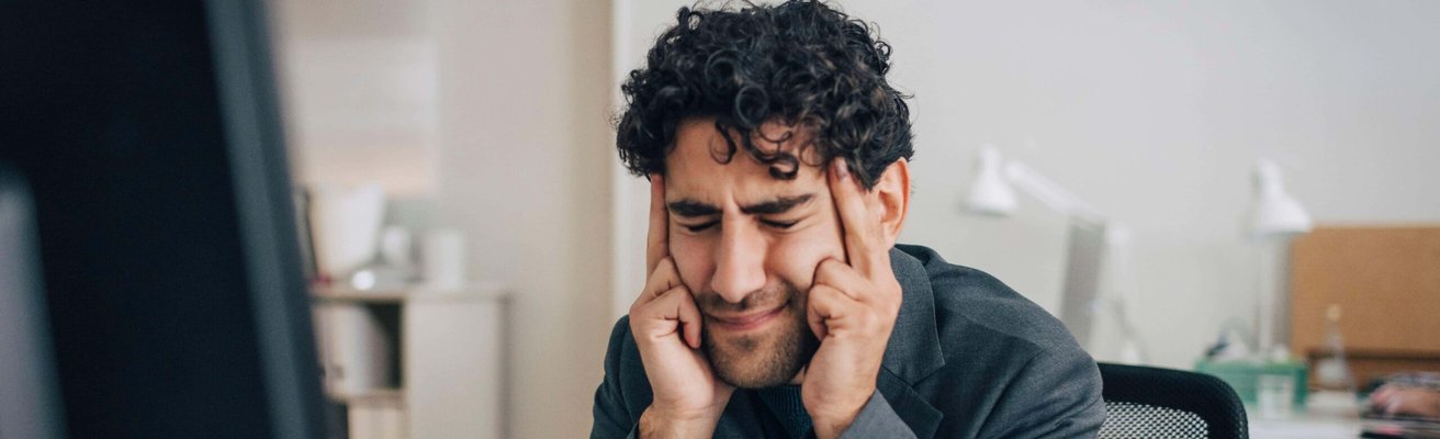 Stressed male entrepreneur touching temples while sitting at desk in creative office