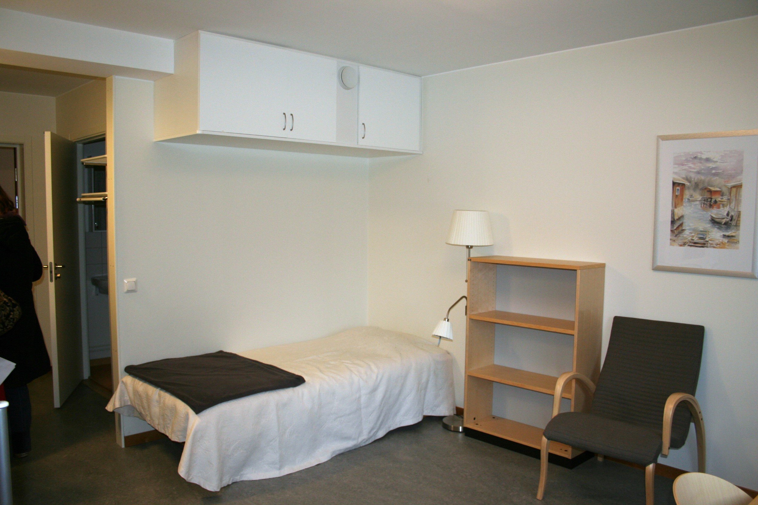 Student room with bed, bookshelf and armchair.