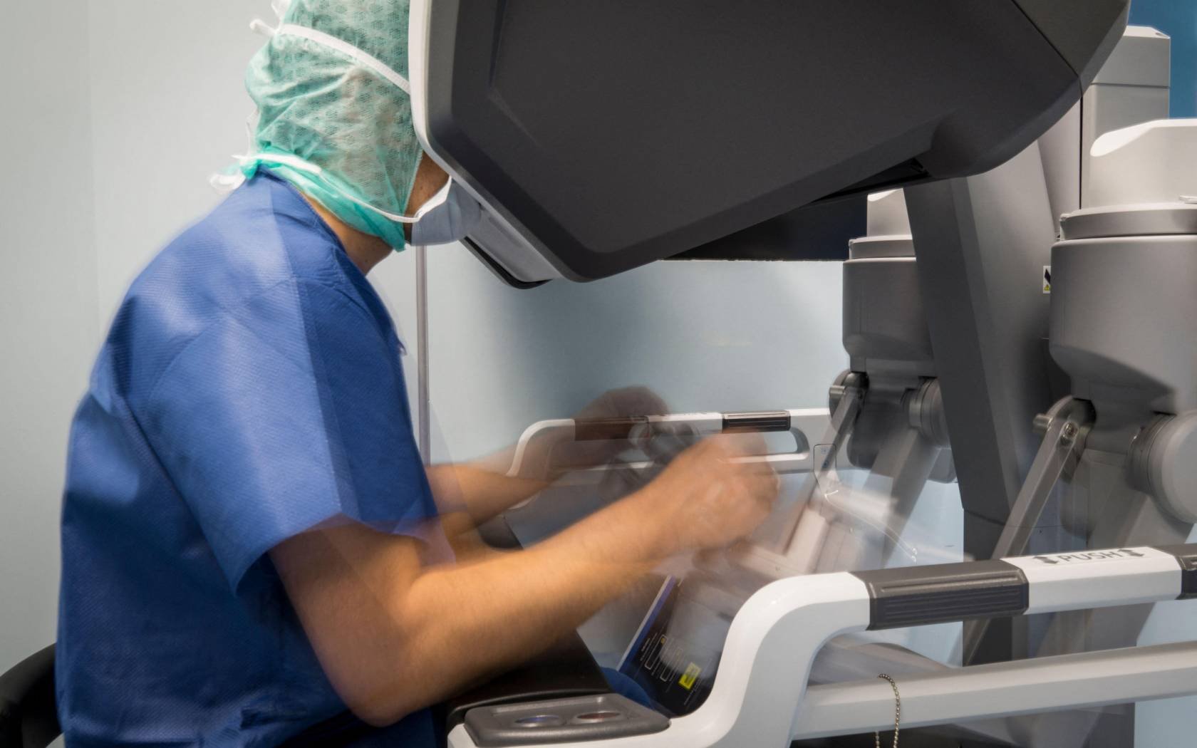 A surgeon manipulates the controls of a robot that operates on a patient.
