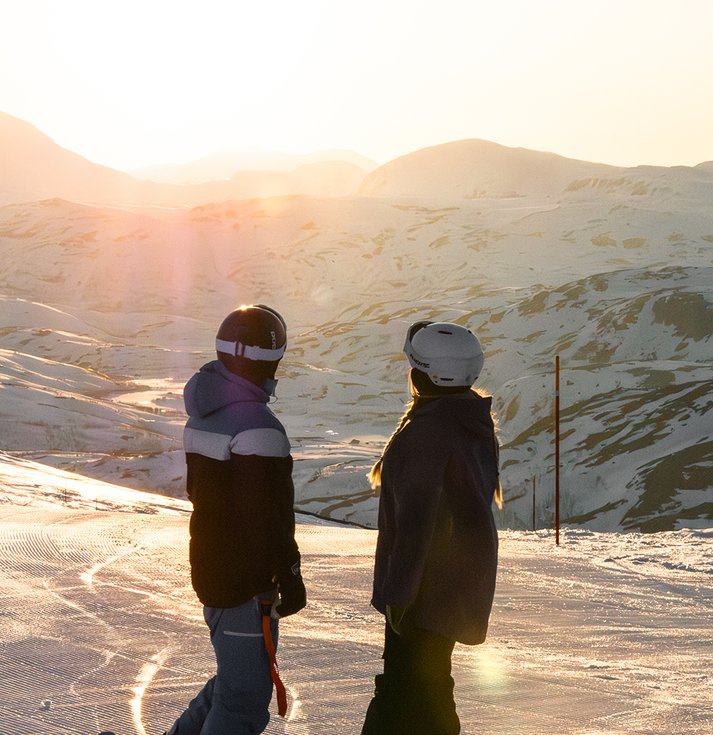 två snowboardåkare kollar på midnattssolen i backen