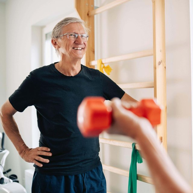 Smiling elderly man standing with hand on hip while talking to male friend in rehab center