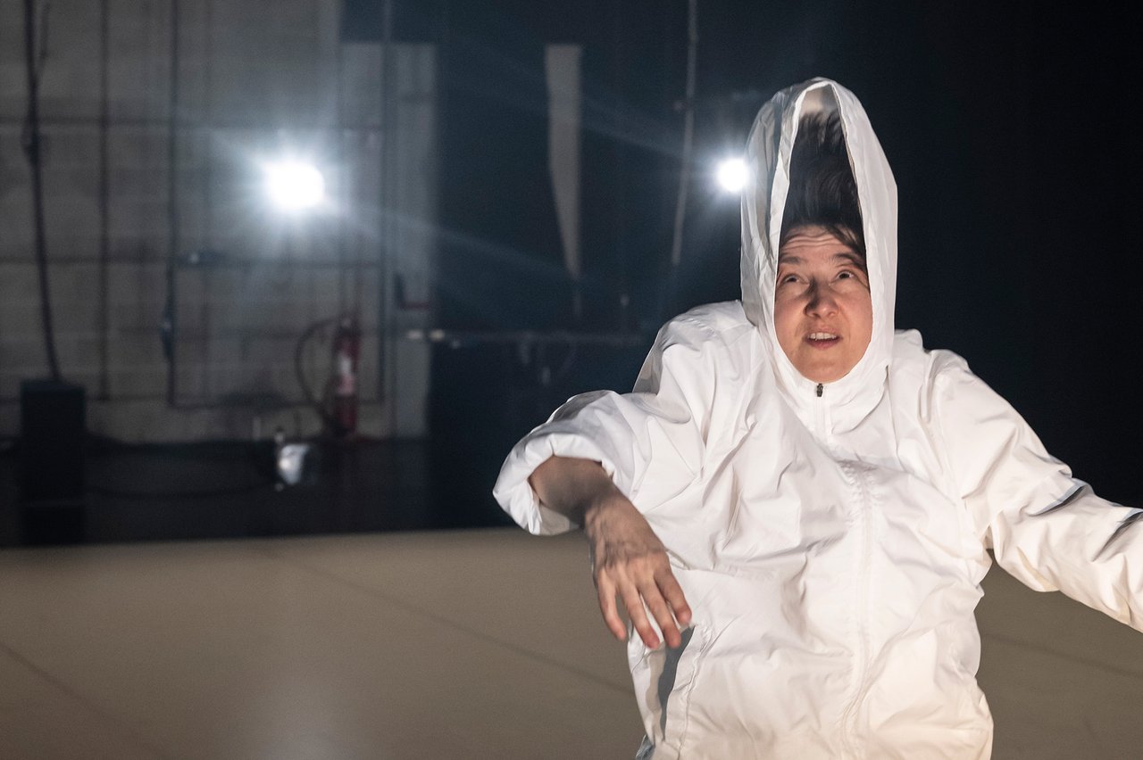 En person i vit luvjacka, shorts och höga strumpor, luvan står upp högt ovanför huvudet.