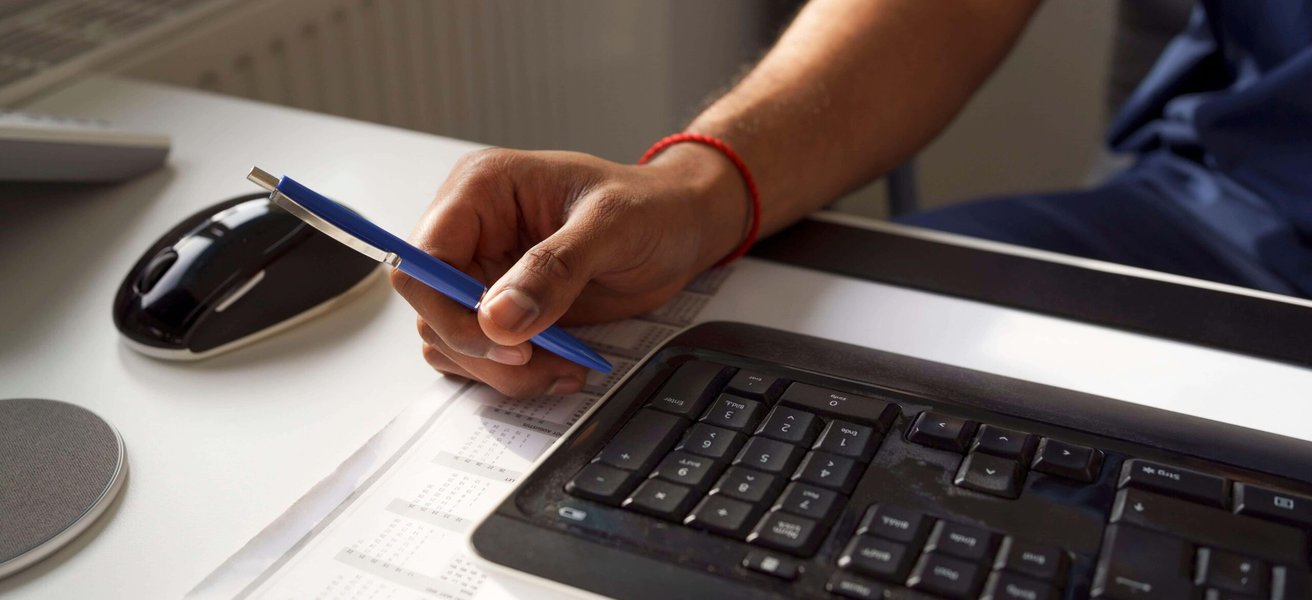 Male healthcare worker holding pen near keyboard at desk in hospital